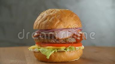 汉堡包在木板上旋转. 一个汉堡和一个切丁色拉奶酪和西红柿围绕着灰色的墙壁。